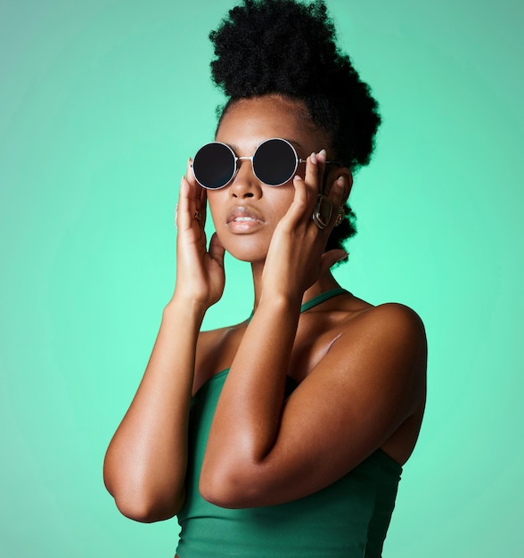 Modna murzynka i okulary z modelką w studio na zielonym tle z okularami przeciwsłonecznymi lub okularami w stylu vintage lub retro Modny styl i pewność siebie z młodą afroamerykanką z afro