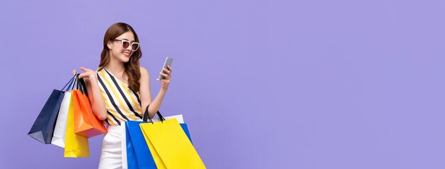 Modna piękna młoda Azjatycka kobieta niosąca kolorowe torby na zakupy online za pomocą telefonu komórkowego
