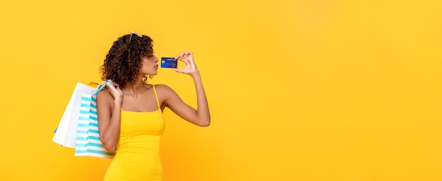 Modne kręcone włosy kobieta niosąca torby na zakupy trzymające kartę kredytową na żółtym tle transparentu z miejscem na kopię