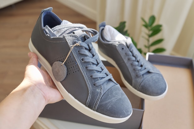 Modne męskie sneakersy z szarej skóry, casualowy design. Nowa para butów wyjęta z pudełka, zakupy online, sezonowe wyprzedaże, trendy obuwia męskiego, pudełko z trampkami w domu