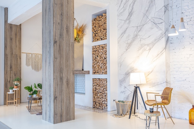 Modne nowoczesne wnętrze jasnej kawalerki z drewnianymi kolumnami w stylu loft, ozdobione cegłą, marmurem i drewnem ze stylowymi meblami i białymi ścianami