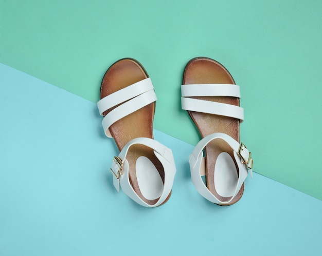 Modne skórzane sandały damskie na kolorowej pastelowej powierzchni, letnie buty, widok z góry, minimalizm