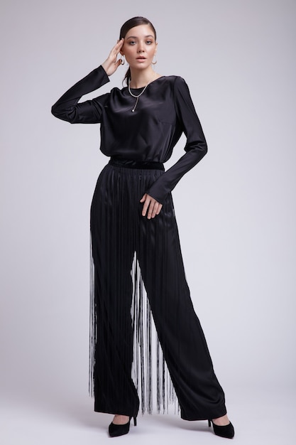 Modne zdjęcie eleganckiej kobiety w czarnej bluzce z frędzlami do spodni na szarym tle