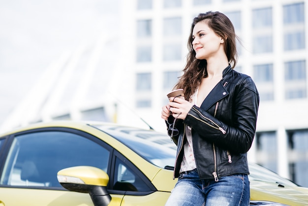 Modnej dziewczyny stojącej w pobliżu samochodu w nowoczesnym mieście