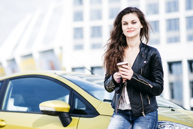 Modnej dziewczyny stojącej w pobliżu samochodu w nowoczesnym mieście