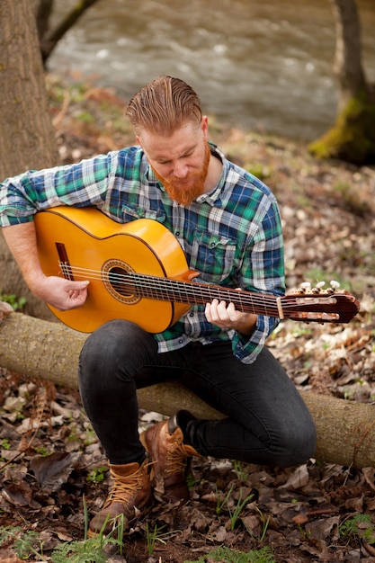 Modnisia mężczyzna z czerwoną brodą z gitarą w polu