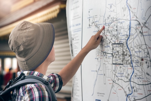 Zdjęcie modnisia podróżnik wskazuje przy miasto mapą z plecakiem