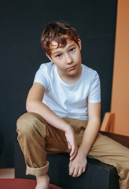 Modny atrakcyjny chłopiec z klatkami piersiowymi o ciemnych włosach, stting na czarnej kostce w studio, modelowanie dla dzieci