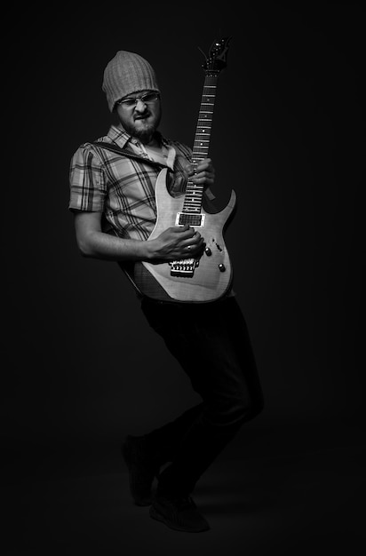 Modny brodaty facet gra na gitarze rockowej na ciemnoszarym tle czarno-białe zdjęcie monochromatyczne