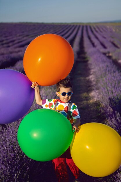 Zdjęcie modny chłopiec w kolorowych ubraniach z kropkami trzyma balon w kwitnącym polu lawendy w letniej osobie