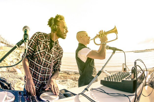 Modny Hipster Dj Grający Letnie Hity Na Imprezie O Zachodzie Słońca Na Plaży Z Wykonawcą Jazzu Na Trąbce