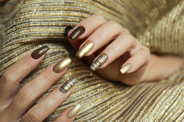 Modny manicure z matowym złotym kolorem lakieru i brązem na długich paznokciach.