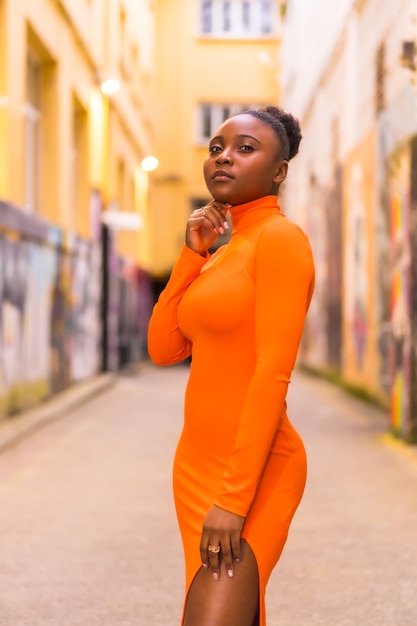Modny miejski styl z czarną Afrykanką w pomarańczowej sukience i czarnych szpilkach