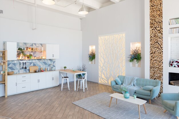 Modny przestronny apartament o stylowym wystroju w pastelowych kolorach zieleni, szarości i bieli z dużym oknem i dekoracyjnymi ścianami. sypialnia i kuchnia