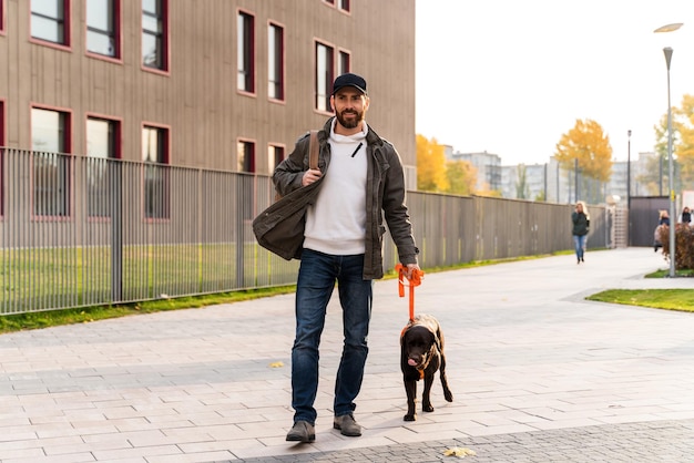 Mój Mądry Chłopak. Szczęśliwy Człowiek Ubrany Na Co Dzień, Trzymając Smycz I Spacerując Ze Swoim Inteligentnym Psem Labradorem, Spędzając Czas Na Ulicy. Zdjęcie Stockowe