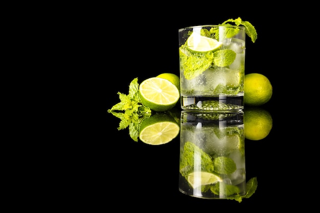 Mojito iz limonką i miętą obok szklanki z odbiciem na czarnym tle