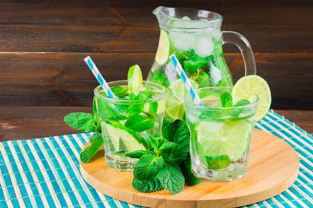 Mojito z miętą i limonką w szklance i dzbankiem na okrągłej planszy. Brązowy drewno tło.