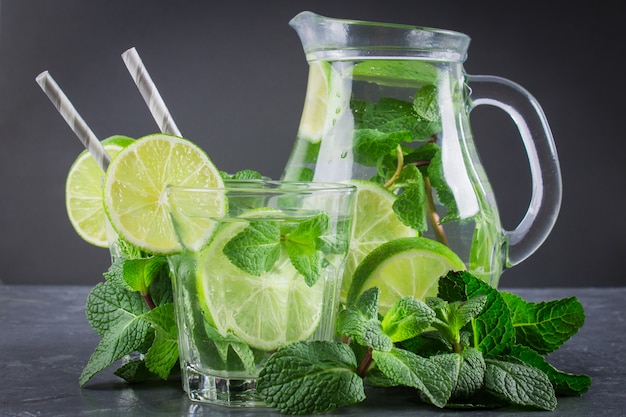 Mojito z miętą i limonką w szklance i dzbankiem z tubkami. Szare tło marmuru.