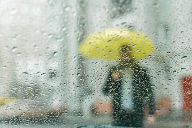 Mokre krople deszczu na szkle. mężczyzna z żółtą sylwetką przez mokre szkło