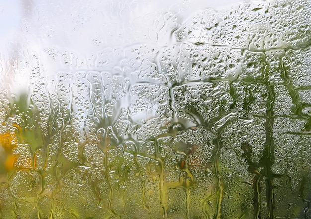 Mokre szkło z kroplami deszczu na tle przyrody.