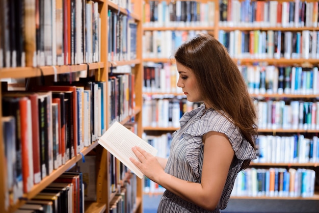 Mól książkowy dziewczyna stoi blisko półka na książki w bibliotece