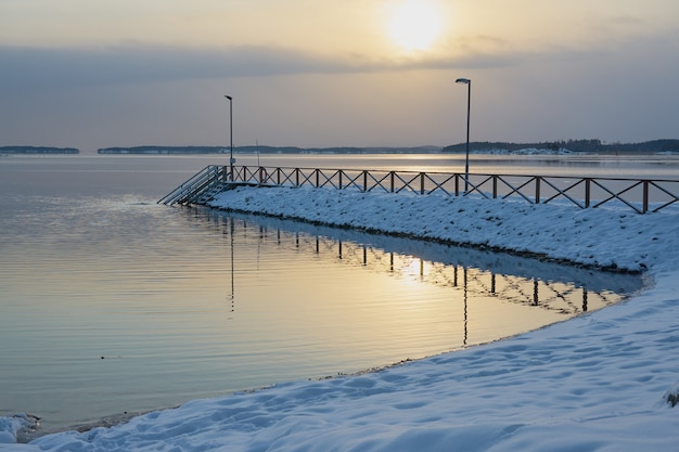 Molo w śniegu o zachodzie słońca na brzegu marznącego morza.