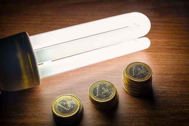 Zdjęcie monety na ciemnej powierzchni z żarówką obok wartości energetycznej i oszczędności energii