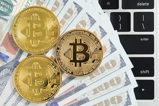 Monety złote Bitcoins i klawiatura komputerowa banknotów US. Zbliżenie metalowych błyszczących monet kryptowalut bitcoin i dolara amerykańskiego