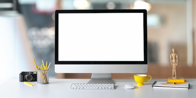 Monitor komputerowy z białym pustym ekranem i kreatywnym wyposażeniem biurowym w przestrzeni roboczej.