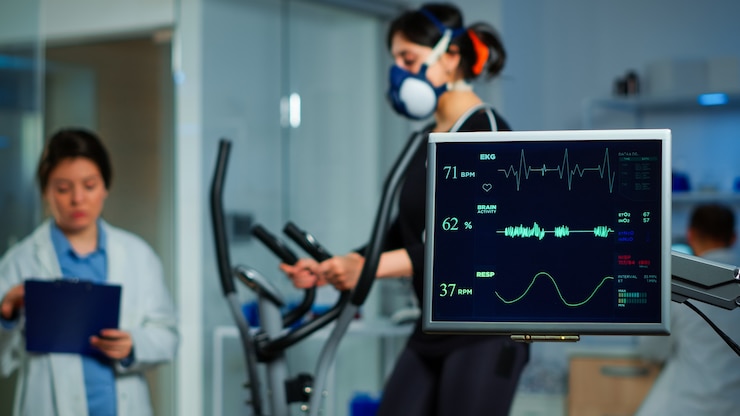 Zdjęcie monitor pokazujący skan ekg sportowca biegającego na orbitreku, a specjaliści medyczni nadzorują ćwiczenia w tle, kontrolują aktywność fizyczną, mierzą tętno w laboratorium nauk o sporcie