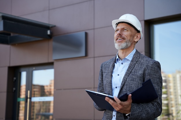 Monitorowanie procesu pewny siebie kierownik inżynier architekt w średnim wieku noszący kask odwracający wzrok