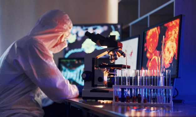 Monitory z informacjami na stole Naukowiec w białym mundurze ochronnym pracuje z koronawirusem i probówkami z krwią w laboratorium