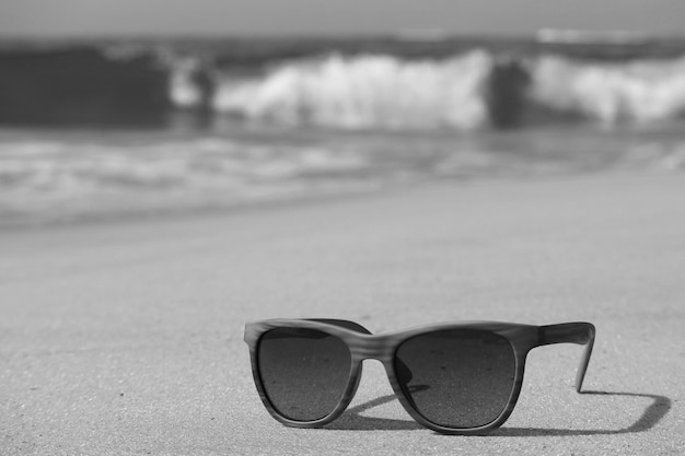 Monotonne okulary przeciwsłoneczne na piaszczystej plaży z rozmytymi falami w tle