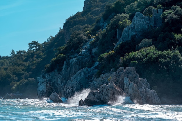 Morskie fale na skalistym, zalesionym wybrzeżu Morza Śródziemnego z ruinami twierdzy