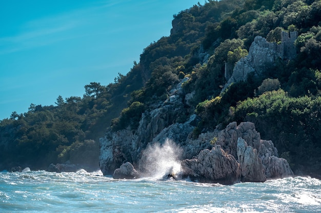 Morskie fale na skalistym, zalesionym wybrzeżu Morza Śródziemnego z ruinami twierdzy