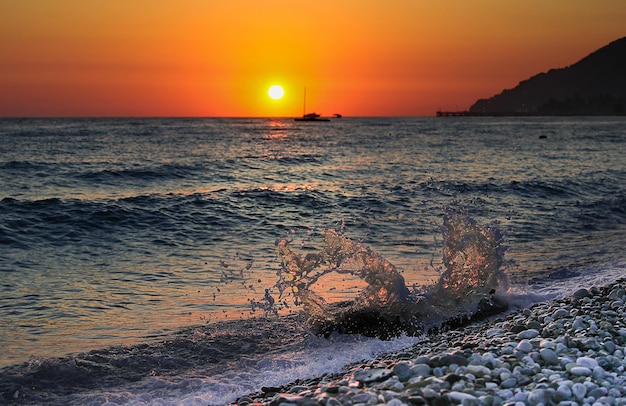 Morze wybrzeże plaża o zachodzie słońca surfowanie w morzu fala z plamami na tle gór kamyki na plaży Koncepcja turystyka urlop podróż krajobraz na pocztówce Zdjęcie wysokiej jakości