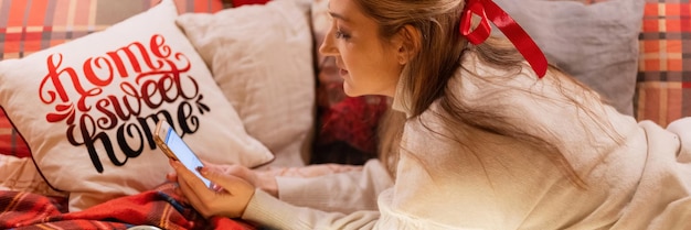 Zdjęcie moskwa 11292021 szczera młoda kobieta komunikuje się z przyjaciółmi za pomocą wiadomości sms na smartfonie w domu w wygodnym łóżku na kocu lub w kratę na szczęśliwego nowego roku i wesołych świąt wigilijnych
