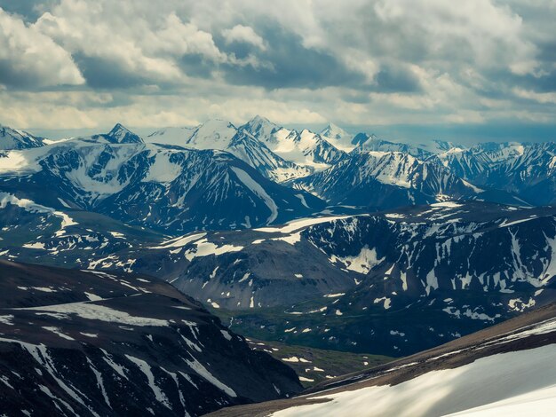 Motley niesamowity widok z lotu ptaka na góry ośnieżone pod zachmurzonym niebem Malowniczy krajobraz górski na dużej wysokości z zachmurzeniem Atmosferyczne tło górskie z pięknym ośnieżonym pasmem górskim