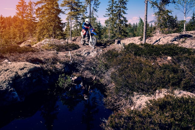 Motocyklista na sportowym motocyklu terenowym enduro jeździ po kamienistej drodze w lesie w wyścigu