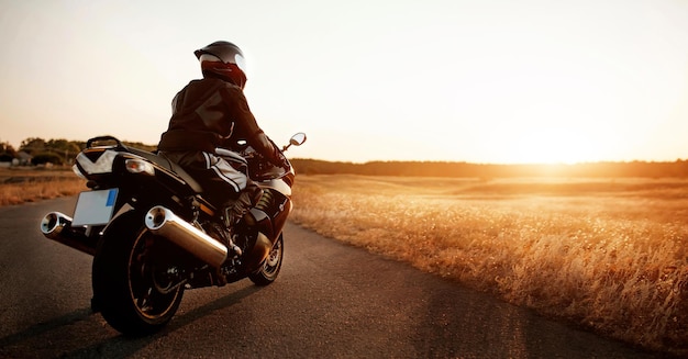 Motocyklista w kasku jeździ po drodze na nowoczesnym czarnym motocyklu. Rower sportowy. Skopiuj miejsce na dostosowany tekst. Motocyklista w skórzanym ochraniaczu