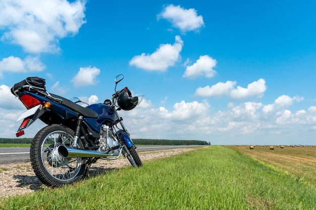 Motocyklowa wycieczka po wsi latem Niebieski motocykl na tle błękitnego nieba i białych chmur
