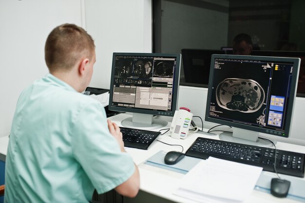 Motyw medyczny. Lekarz w gabinecie rezonansu magnetycznego w centrum diagnostycznym w szpitalu, siedząc w pobliżu monitorów komputera z ludzkim mózgiem.