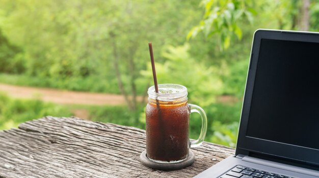 Mrożona kawa americano i laptop na drewnianym stole.