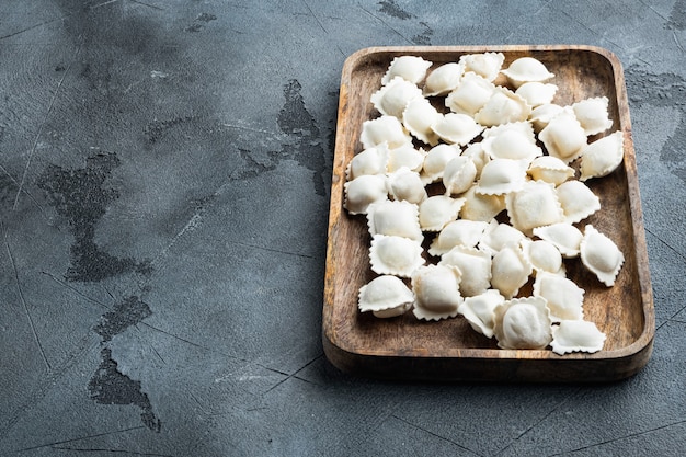 Mrożone pierogi z tortellini i ravioli w drewnianym pudełku, na szarym tle