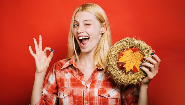 Mrugająca kobieta w szkockiej kraty koszula z dekoracyjnym jesiennym wiankiem szczęśliwa dziewczyna pokazuje ok znaka