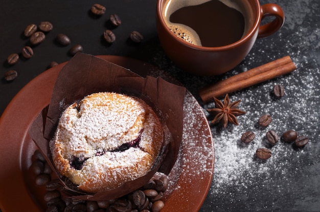 Zdjęcie muffin z jagodami w brązowym talerzu i filiżanką gorącej kawy na czarnym tle