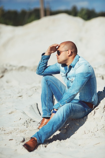 Mulat opalony siedzi na piasku w okularach