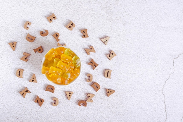 Zdjęcie multivitaminy do żucia w postaci niedźwiedziek cukierkowych w misce i drewnianych liter z góry