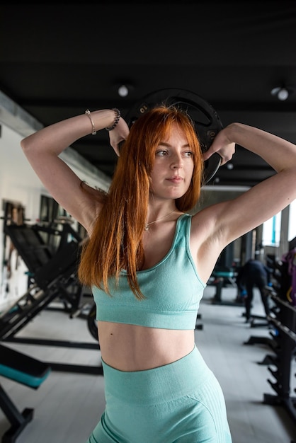 Muskularna młoda kobieta podnosząca ciężki talerz lub dysk na siłowni