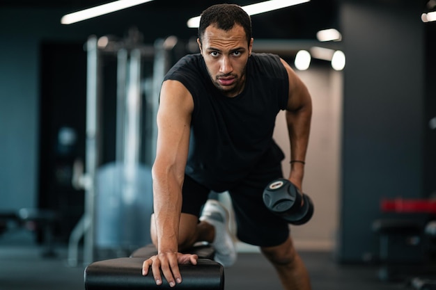 Muskularny afroamerykanin robi trening bicepsa z hantlami w siłowni